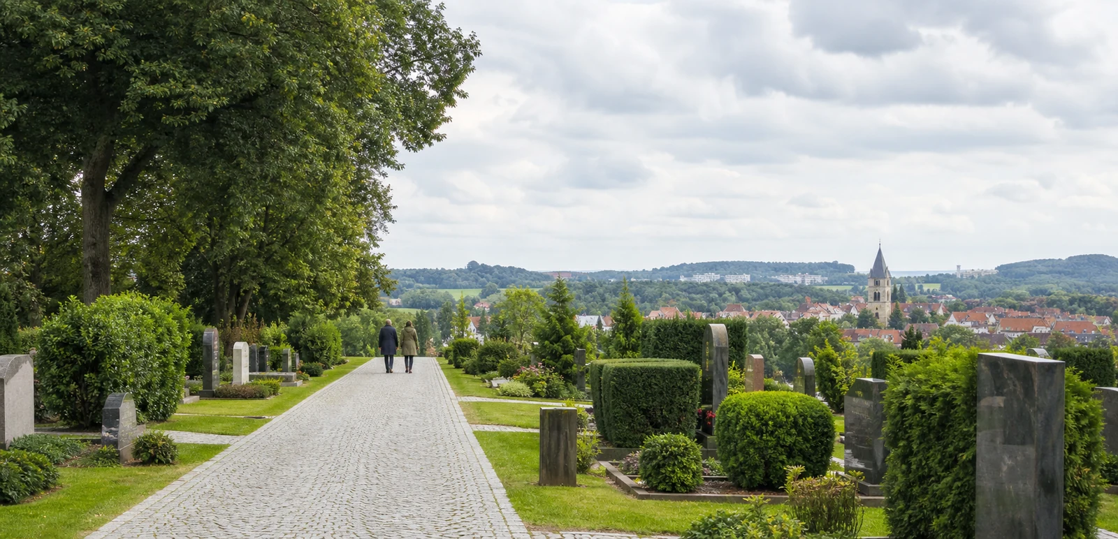 Heller Weg durch einen gepflegten Friedhof mit einer Stadt im Hintergrund